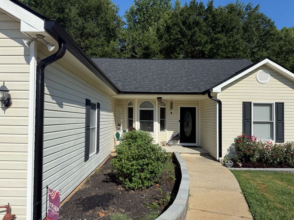 A single story house with dark asphalt shingle roofing, black gutters, and cream vinyl siding.