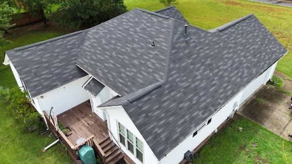 Aerial view of a house with gray architectural asphalt shingles, white siding, and a wooden deck below.