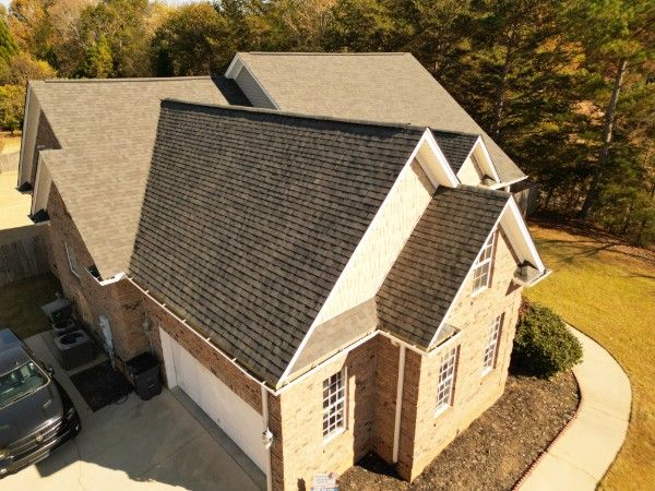 Aerial view of a brick house with asphalt shingle roofing, multiple gables, and white trimmed gutters.