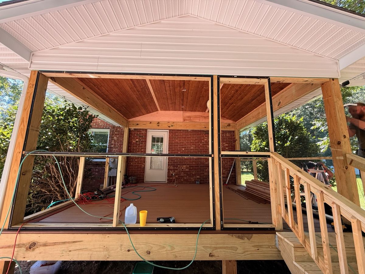 A screened porch addition with wood plank ceiling, composite decking, and new stairs against a brick house.