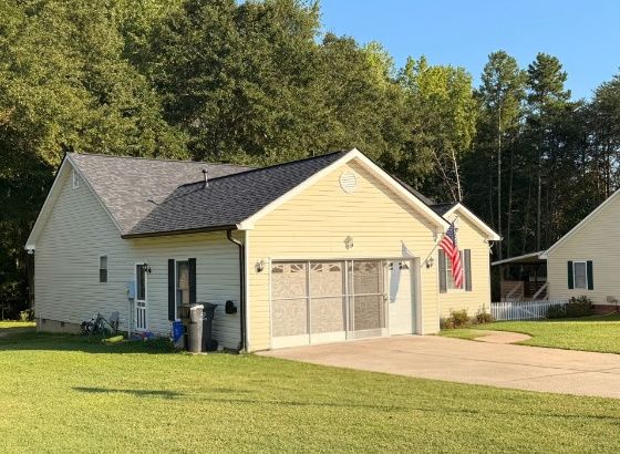 Single story yellow vinyl siding home with a dark shingle roof and attached garage with concrete driveway.